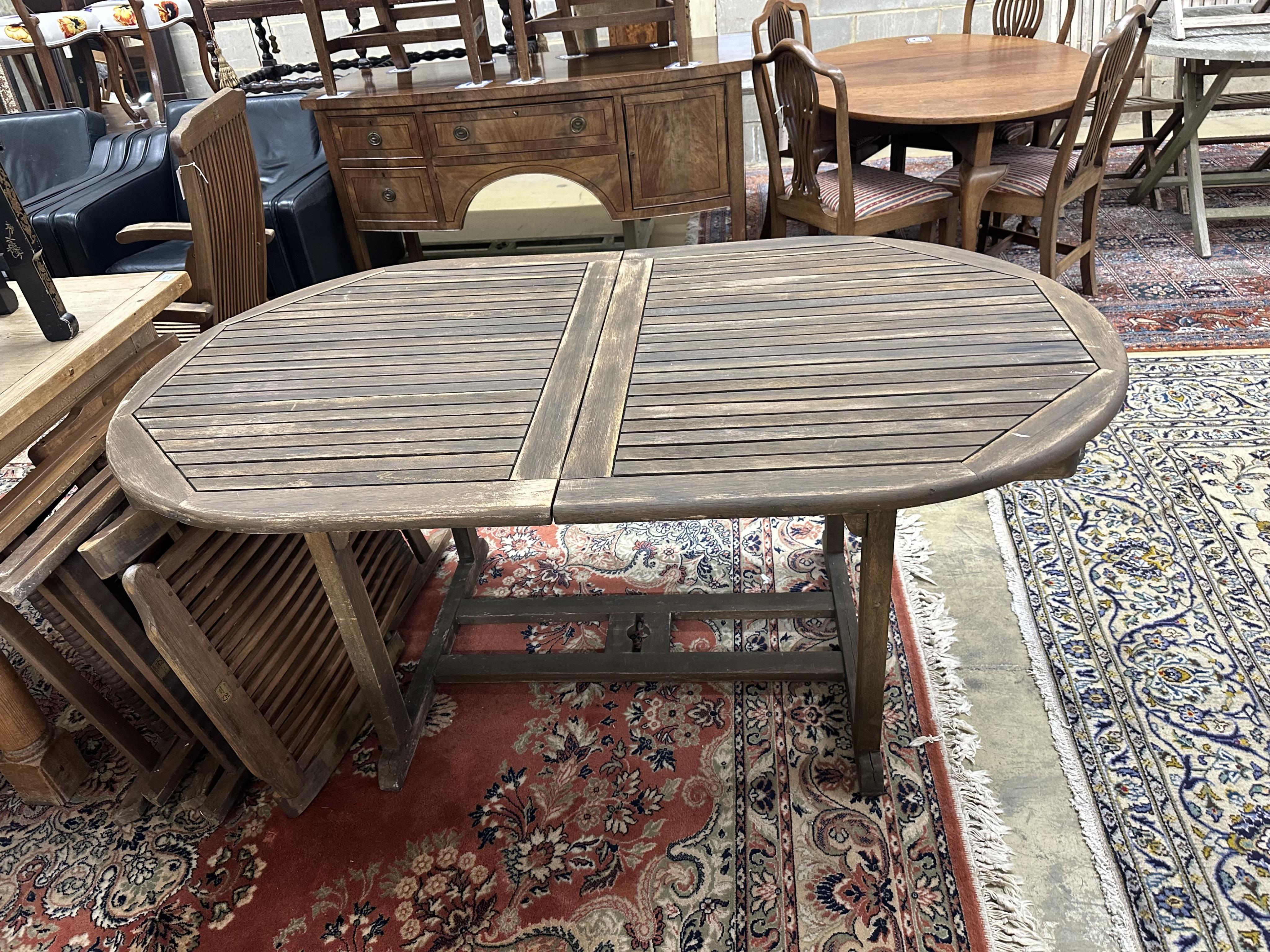 A weathered teak extending garden table, approximately 220cm extended, depth 100cm, height 74cm, together with six teak folding garden armchairs. Condition - fair